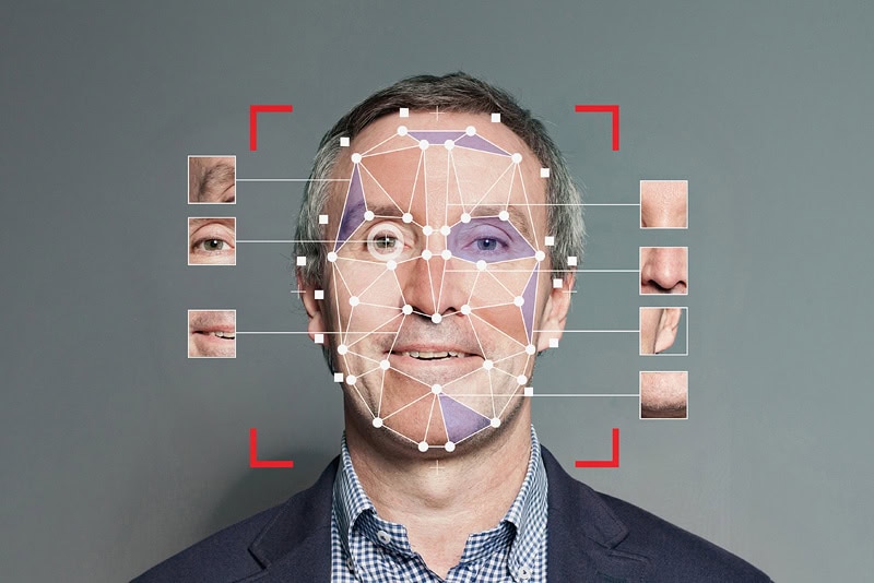 A middle-aged caucasian man in a suit jacket and checkered shirt stands against a gray background, with his face partially overlaid by an AI headshots facial recognition grid and various facial feature close-ups.